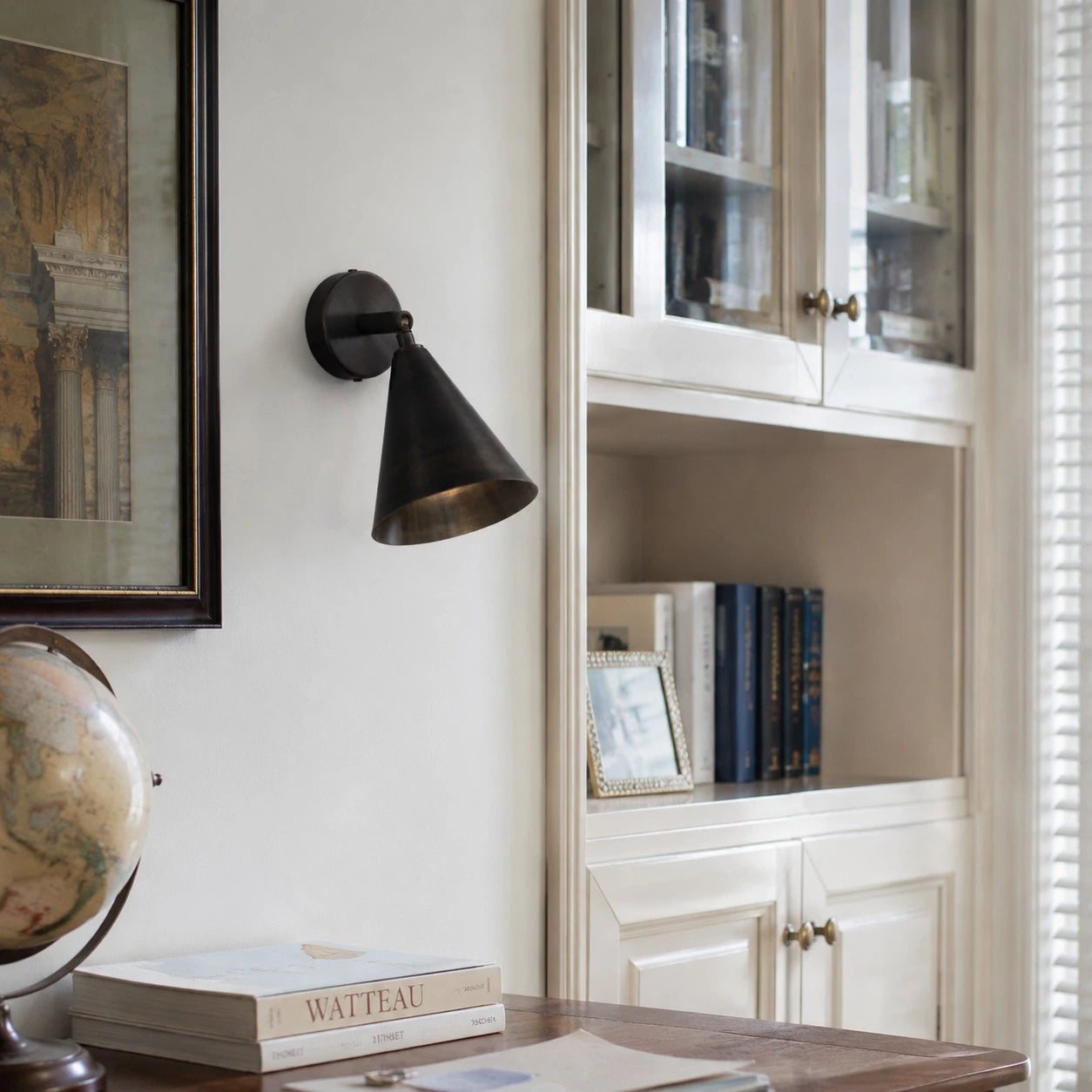 Matte black brass wall light above books and a desk corner