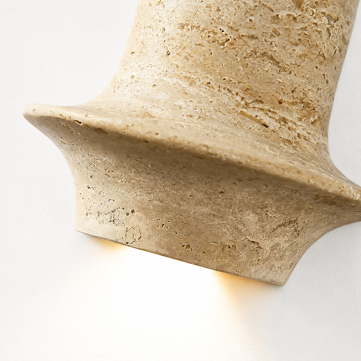 Lit close view of travertine wall lamp showing warm downward glow and honed stone edge