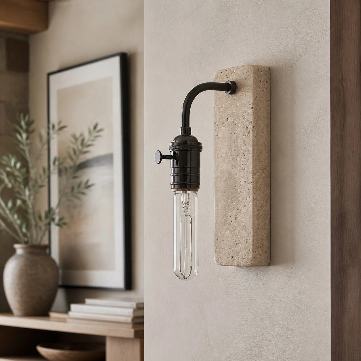 Black travertine wall sconce beside framed art and natural decor