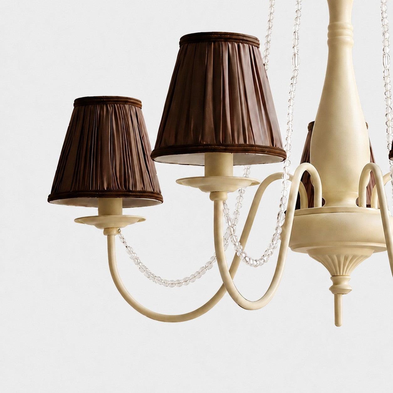 Close-up of cream iron chandelier body with curved arms and bead trim