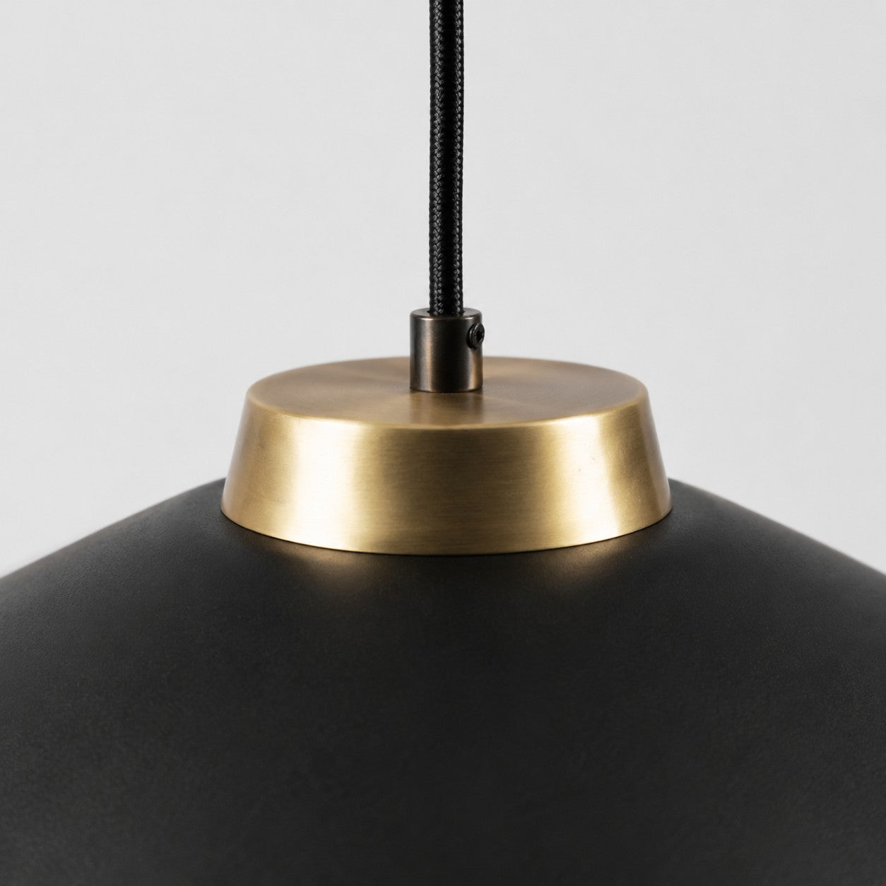 Close view of the black braided cord and brushed brass shade connector
