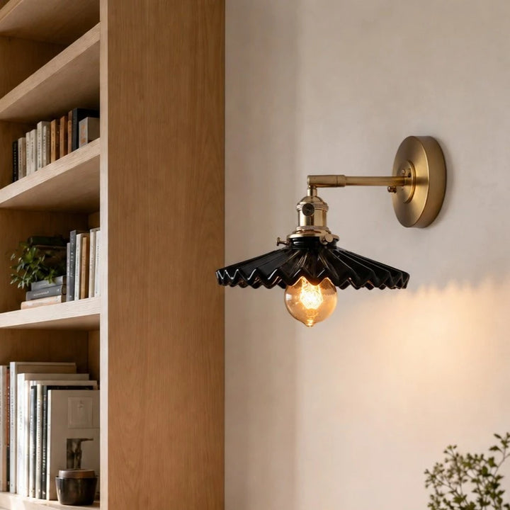 Black pleated ceramic wall sconce installed near a bookshelf