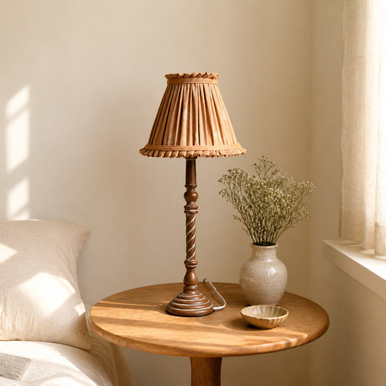 Warm tan pleated table lamp beside window in soft home corner
