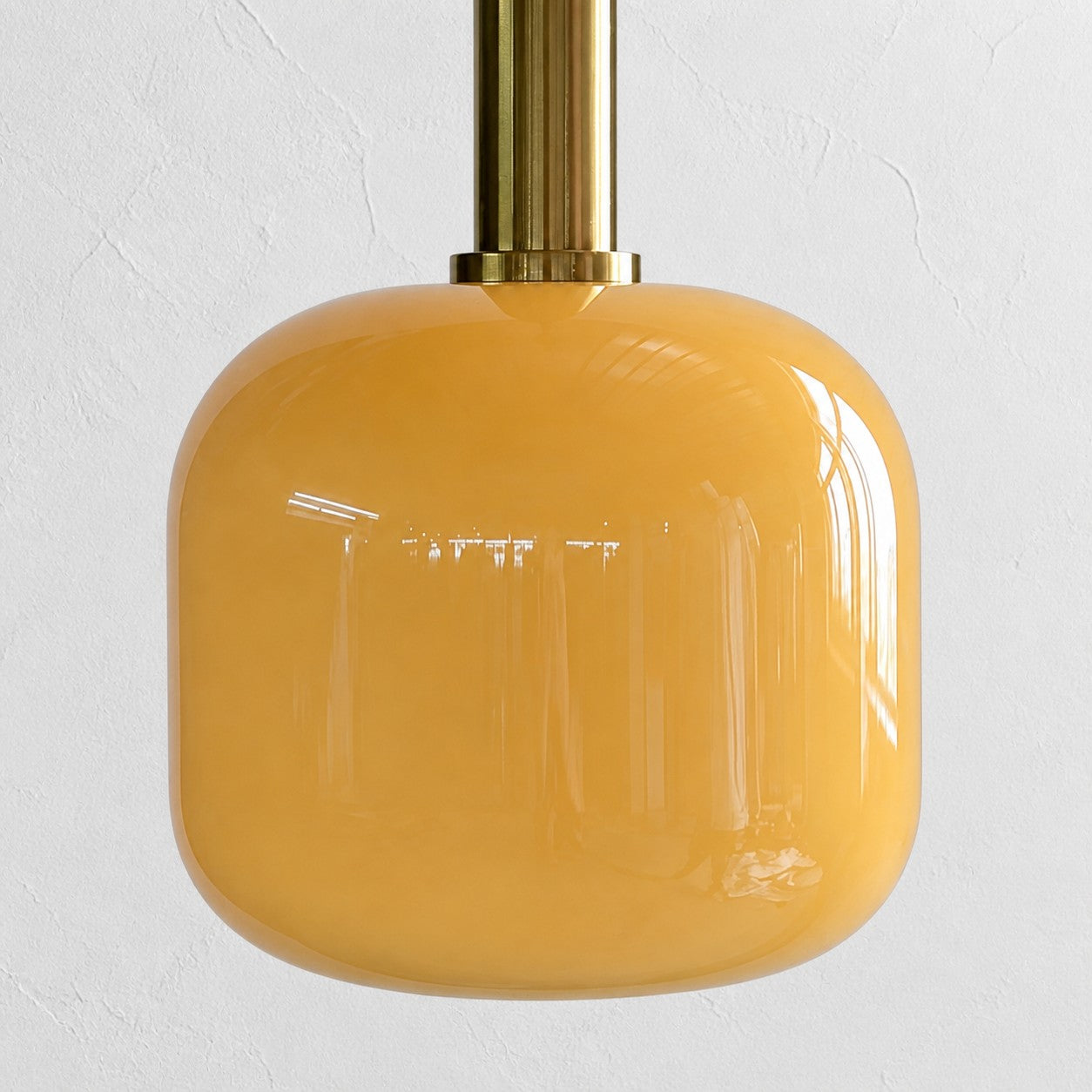 Close view of the rounded glossy yellow glass shade and brass holder